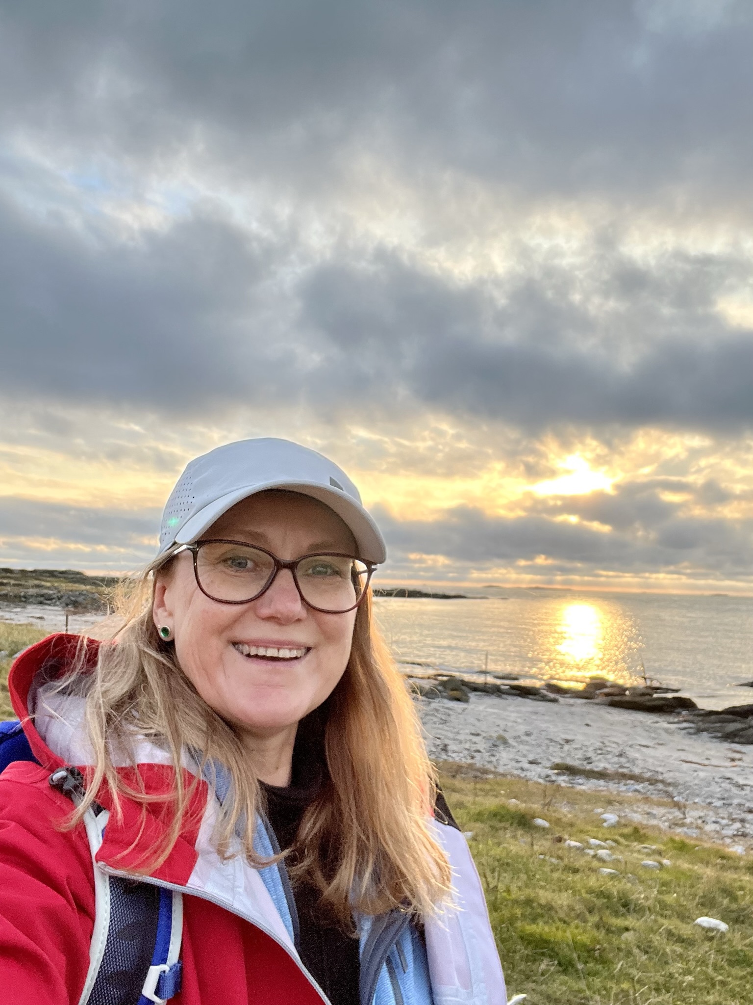 Bilde av Kristine Enger med Molvika i bakgrunnen. Solen skinner gjennom skydekket og glitrer i sjøen.